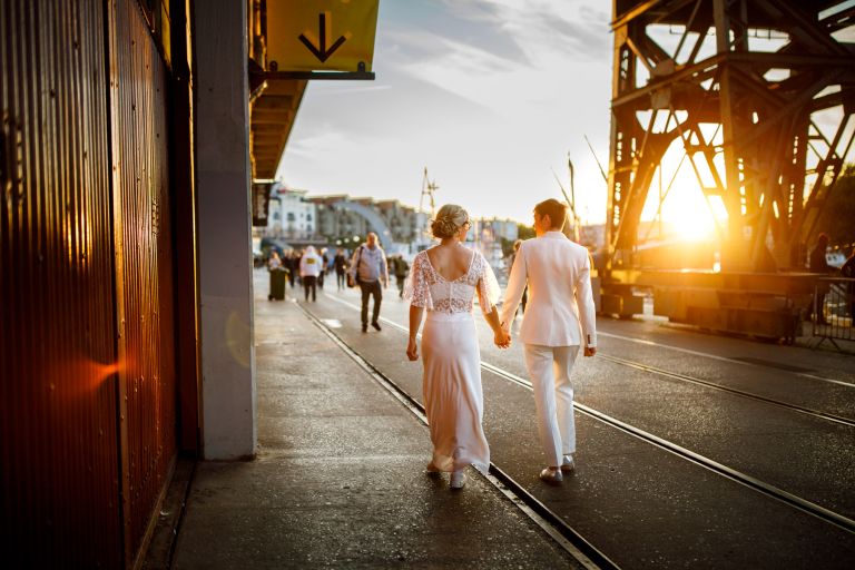 Two brides hold hands and walk into golden hour light Bristol same sex wedding