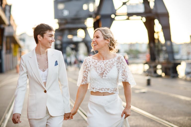 Two stunning brides walk during golden hour smiling at each other in central Bristol wedding