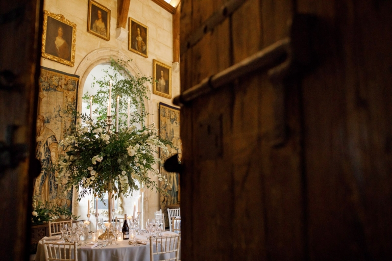 beautiful table flowers at english castle surrounded by very old portraits as seen through the big castle door