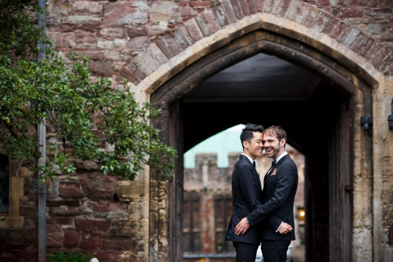 Berkeley Castle Wedding - same sex wedding - two grooms hug in front of castle archway
