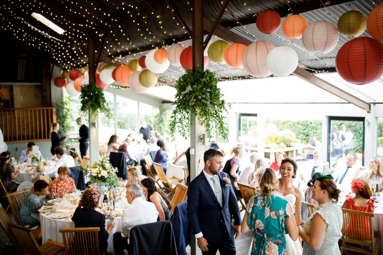 Room view of guests enjoying themselves during meal at cripps stone barn wedding photos. Wedding decor of lots of coloured lanterns and fairy lights