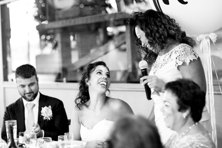 bride and her sister smile at each other during speech at stone barn