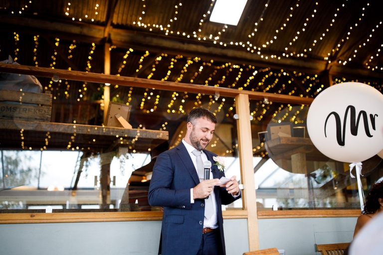Groom gives speech with fairy lights in the background at stone barn wedding photos