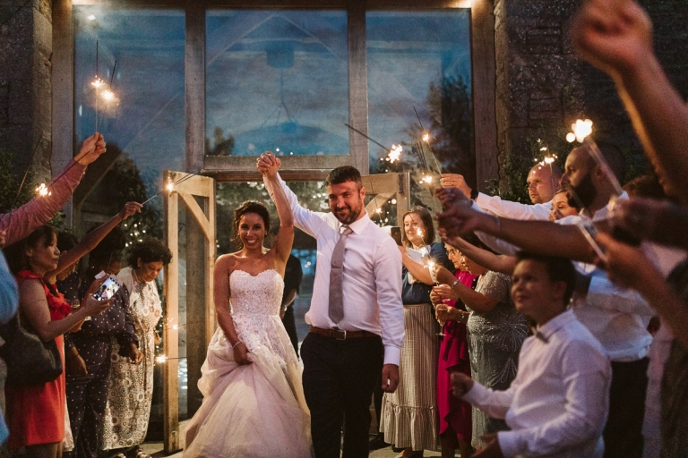 Couple hold hands in the air during sparkler exit at cripps stone barn