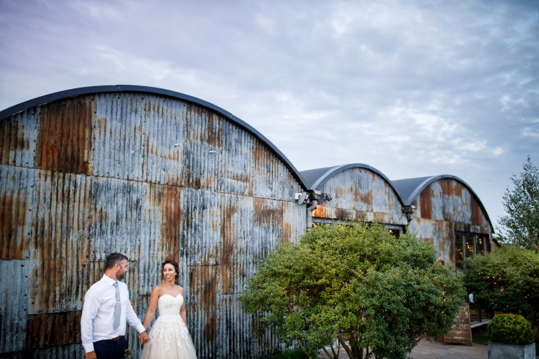 Stone Barn - Couple stood outside the corrugated iron front of the barn. Blog featuring their wedding in an English Barn in the Cotswolds.