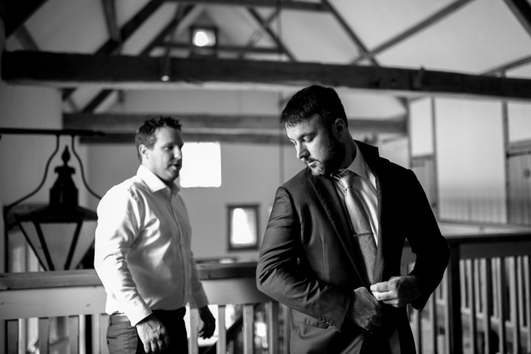 Groom puts on his jacket before stone barn wedding