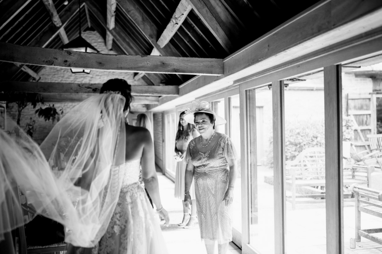 brides mum sees her for first time before wedding at stone barn. Bride has long cathedral length veil. 