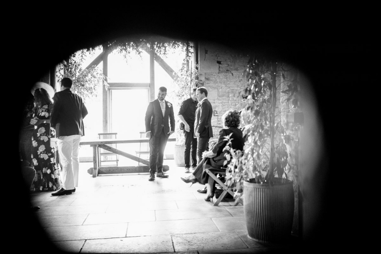 Groom before ceremony as seen through hole in old door at cripps stone barn