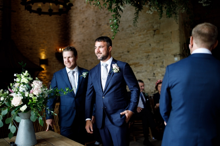 Groom and groomsmen wearing dark blue suits with light blue ties waits for bride at Cripps Stone Barn