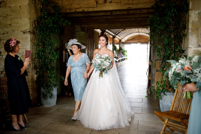 Bride walked in by Mum who is wearing light blue mother of the bride outfit at Stone Barn