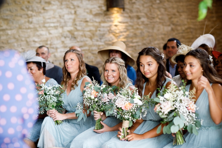 Bridesmaids wearing their light blue bridesmaids dresses carrying their bouquets full of roses and fern during the ceremony at cripps stone barn