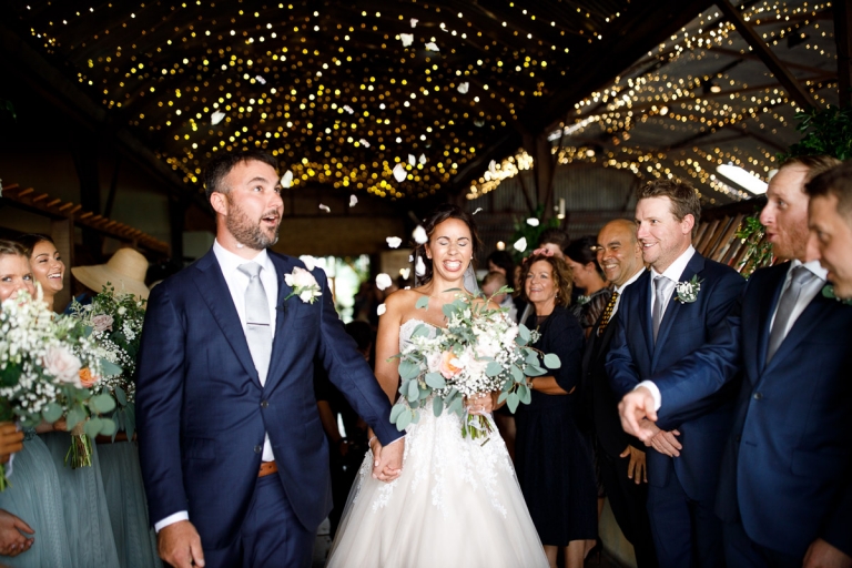 Confetti thrown at Couple with fairy lights in the background at Stone Barn