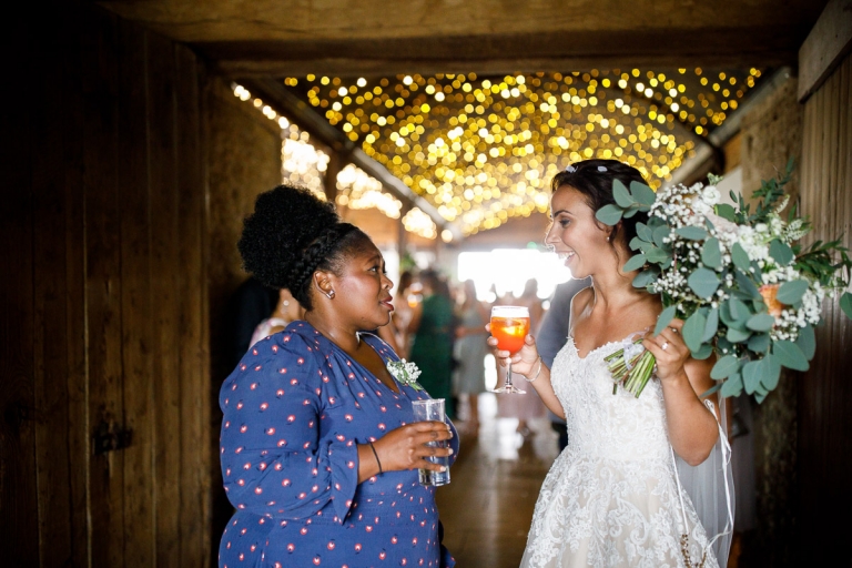 Bride chats to guest at Stone Barn with fairy lights in the background