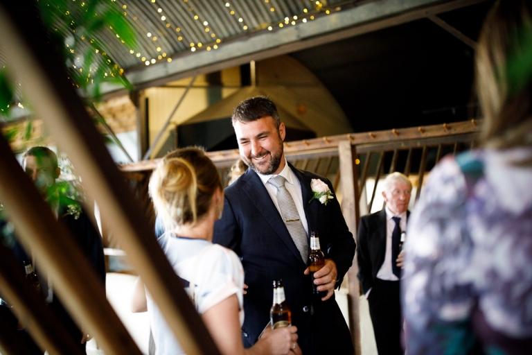 Groom in dark blue wedding suit with a rose button hole chats to guest at wedding at Stone Barn
