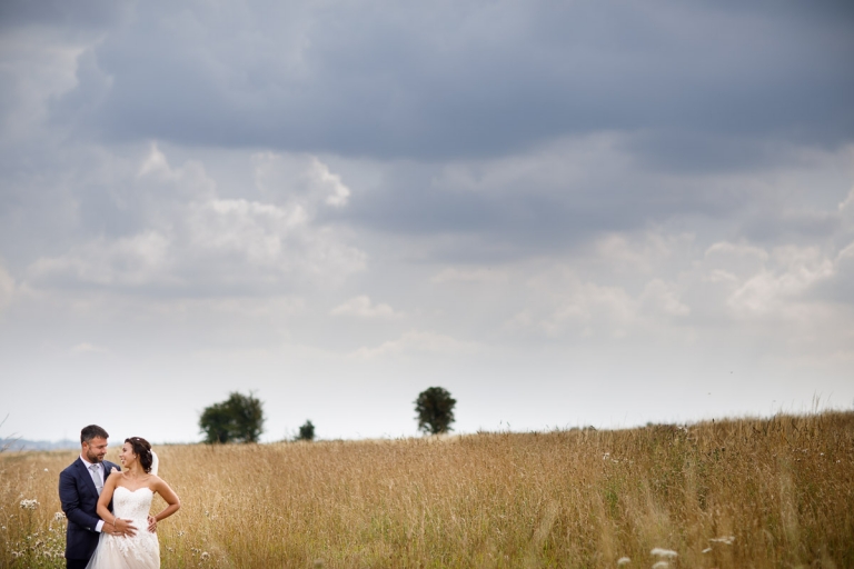 Couple stand in tall grass at wedding at stone barn