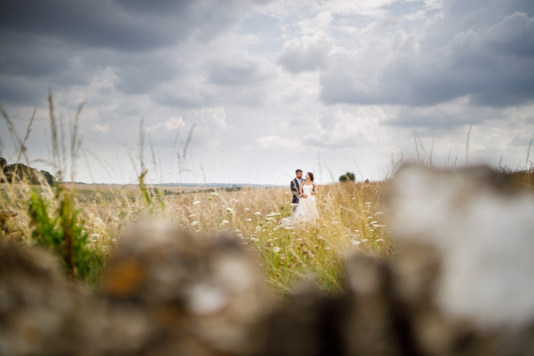 Couple in a field of long grass in their outdoor wedding photos with Cotswold stone wall in the foreground at Stone barn