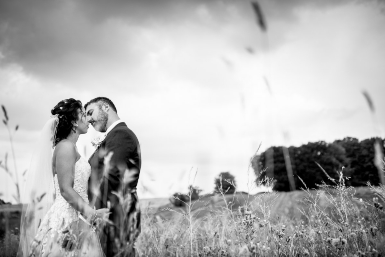 couple kiss in black and white in long grass at stone barn. Outside wedding photos. 