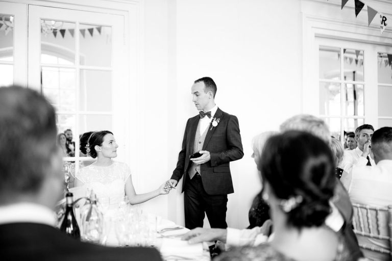 groom holds brides hand as he speaks about her during his wedding speech in the orangery at goldney house