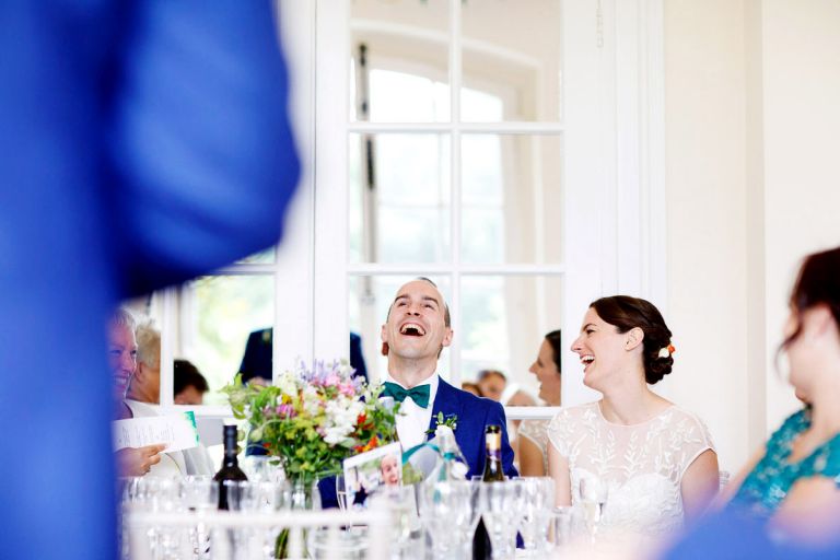 bride and groom laugh at the bestmans speech, bride looks at the groom as they do as the joke is at his expense