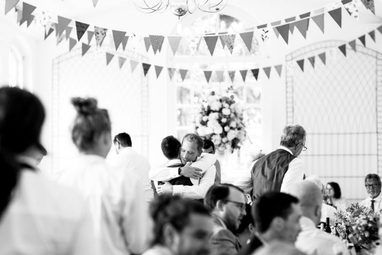groom hugs his best man after the speeches at the orangery at goldney house bristol, lots of bunting hanging above them