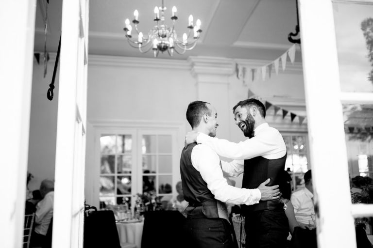 groom is laughing with one of his ushers at his wedding after the speeches in black and white