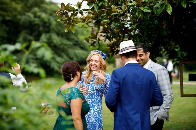 wedding guest in blue with blue flowered headband laugh at something a bridesmaid says to her in the trees outside in clifton