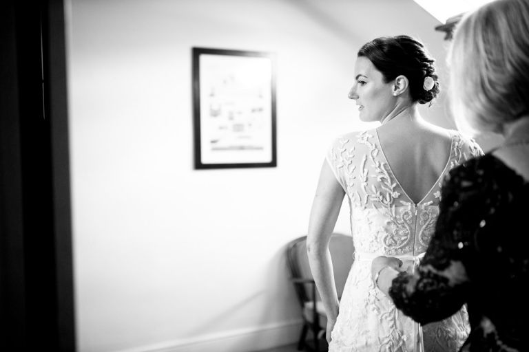 black and white photo of bride having her dress done up by her mum before wedding at goldney house
