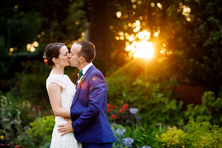 Sunflare and sun beams through the trees, golden in colour, there is lens flare which is over the kissing wedding couple outside at goldney hall