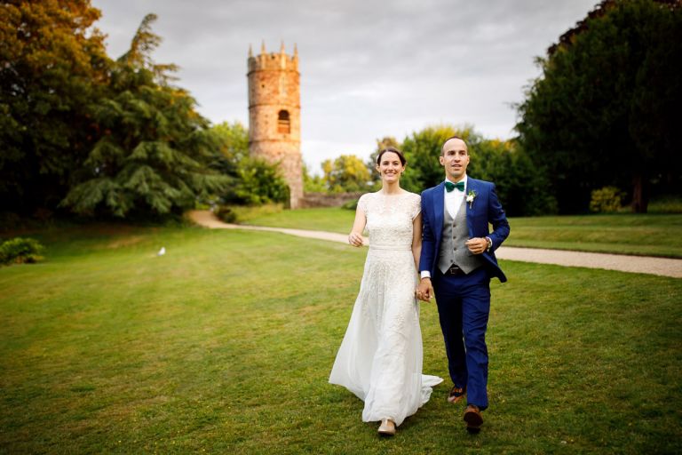 Couple run back to their party at goldney hall with the sun hitting the tower in the background and the cat is in the distance