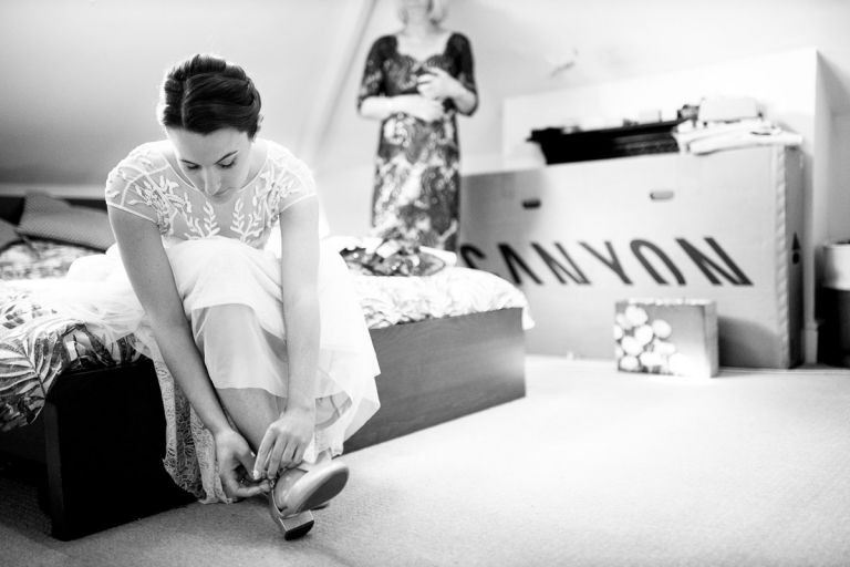 bride doing up her wedding shoes sat on the edge of her bed before going to her ceremony at goldney house