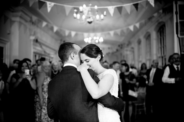 Couple have first dance in the orangery at goldney hall, they hug and their guests are behind them
