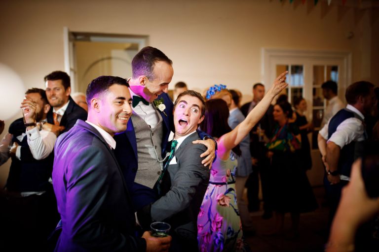 groom is lifted in the air by his friends while dancing in the orangery in bristol, they smile for a guests camera