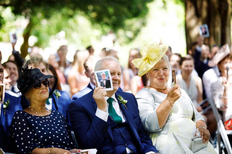 grooms parents hold up photos during a game in their sons wedding ceremony at goldney house
