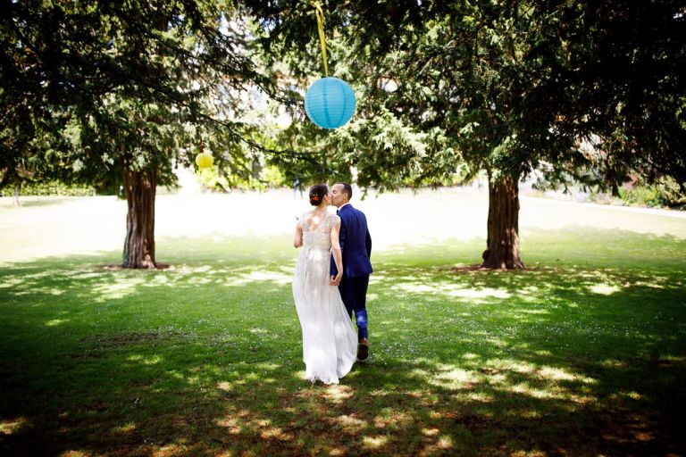 Couple kiss under the trees with single central blue lantern above them as they exit their wedding ceremony outdoors at goldney house