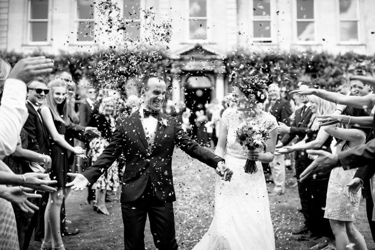 Couple laugh and squint as lots of confetti in thrown in their faces at goldney hall