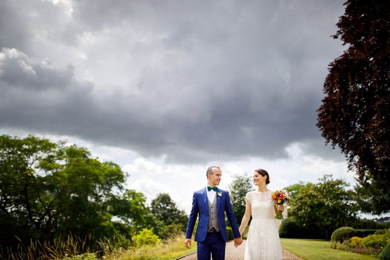 Couple walk along hand in hand in the sunshine with dark rain clouds behind them, outside in bristol