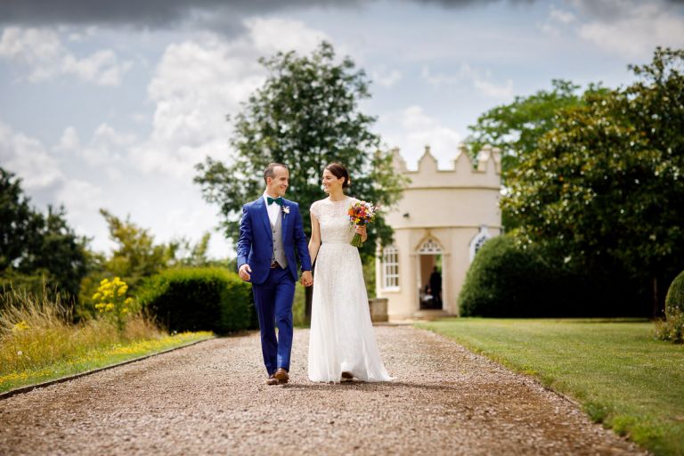 Couple walk along smiling and holding hands, bride holds wedding bouquet in bristol