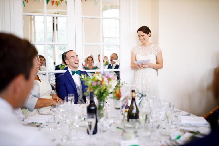 bride gives a speech at wedding at goldney hall in the orangery, the groom laughs as she speaks about him