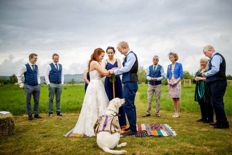 Bridesmaids joins in with handfasting while their dog sits at their feet wanting in on the action, wedding party watch. 