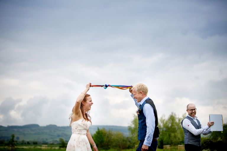 Couple tie the knot after their handfasting during their humanist ceremony, the ribbons are rainbow coloured and the couple are ecstatic, 