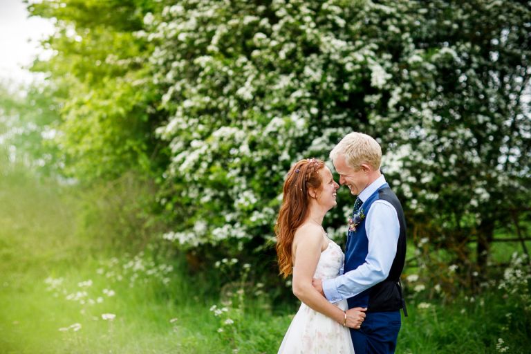 Couple smile at each other in front of blossom with green in the foreground