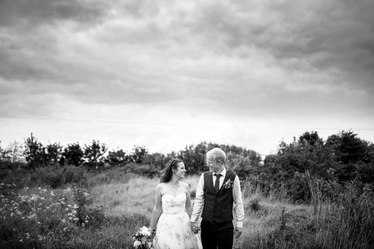 Black and white photo of wedding couple walking through a wild field of flowers