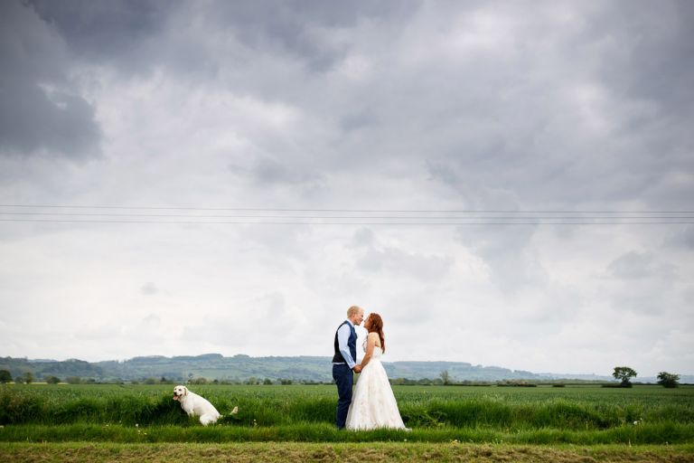 Couple kiss with hills in the background while their dog goes to the toilet right next to them