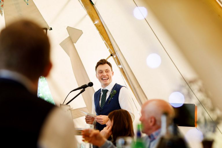 Bestman laughing during his speech about the groom, fairy lights in the foreground