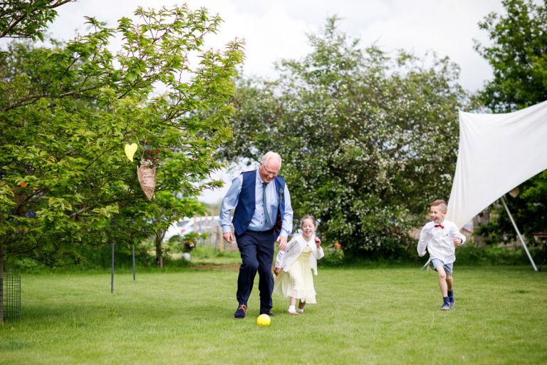 Man is playing football with kids during a wedding reception, all are laughing. 