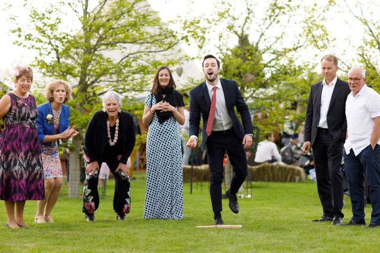 Guests cheer on man who is very happy with his throw during game at wedding