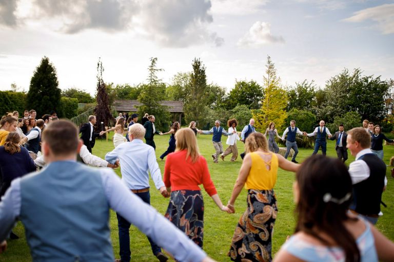 All guests at wedding joins hands in a circle during outside ceilidh 