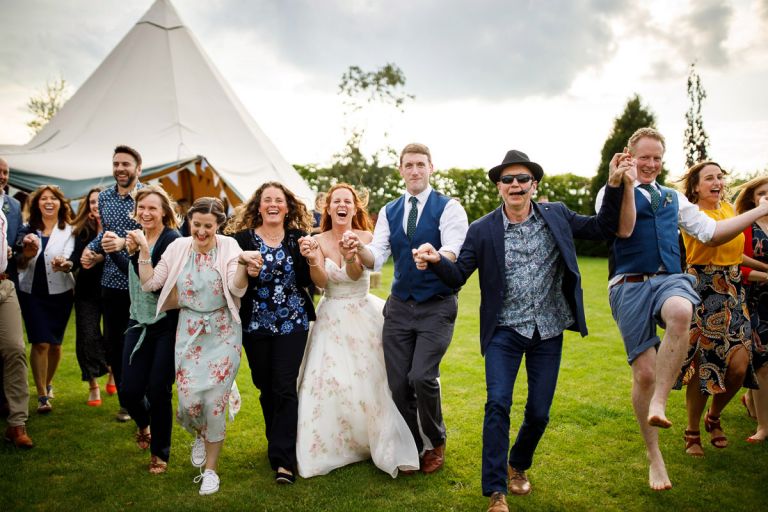 Guests hold hands and run inwards towards the camera laughing during outside ceilidh 