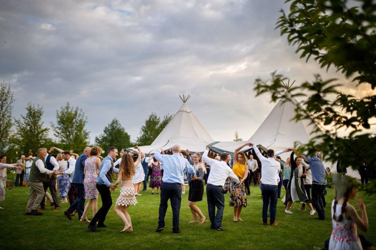 Guests dancing outside with tipi in the background and the sun starting to set 