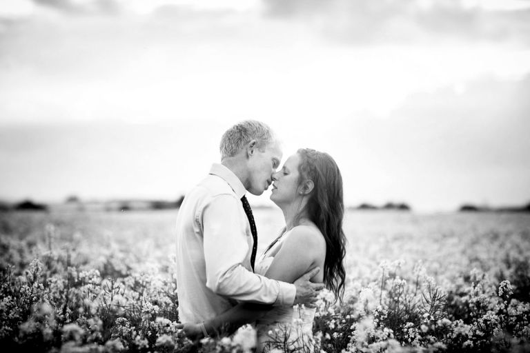 Black and white photo of couple embracing in a field of flowers in the evening of their humanist outside wedding